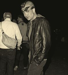 black and white photograph of man in leather jacket looking at his cell phone while standing next to other men