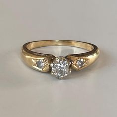 a three stone diamond ring on a white surface with gold band and two diamonds in the middle