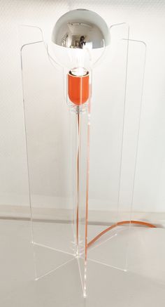 an orange and white lamp on top of a glass stand with a light bulb in the middle