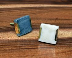 two square shaped marble cufflinks sitting on top of a wooden table next to each other