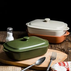 two green casserole dishes with spoons on a cutting board next to an empty bottle