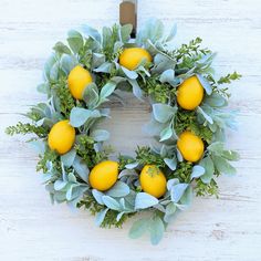 a wreath with lemons and green leaves on a white wooden background is hung on the wall