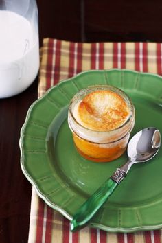 a green plate topped with an orange pie next to a cup of milk and a spoon