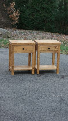 two small wooden tables sitting on the side of a road in front of some trees