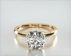 a yellow gold engagement ring with a round cut diamond in the center, on a white background