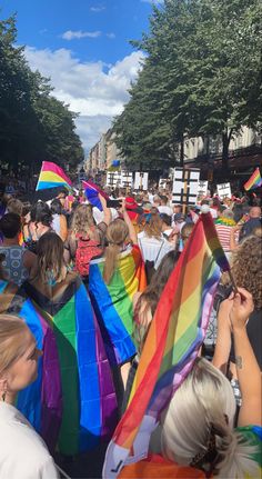 a large group of people walking down a street with rainbow flags on their heads and shoulders