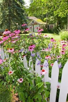 a white picket fence surrounded by flowers and trees