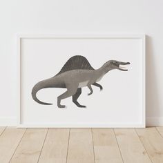 an image of a dinosaur print in a white frame on a wooden floor next to a wall