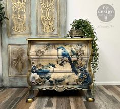 an old dresser with blue and white birds painted on the drawers, next to a potted plant