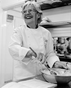 a woman in a chef's uniform is preparing food on a counter top and smiling at the camera