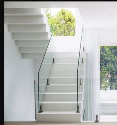 a white staircase with glass railings leading up to the upper floor