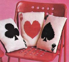 three pillows with black and white designs on them sitting on a red chair in front of a pink wall