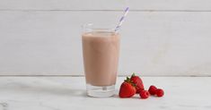 two strawberries sit next to a glass of milkshake