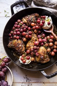 a skillet filled with meat and grapes on top of a white table next to other foods