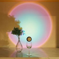 two wine glasses and a vase with flowers in front of a rainbow - colored background