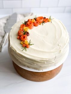 a white frosted cake with orange and yellow flowers on it's top sitting on a table