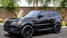 a black range rover is parked in front of a building with trees and bushes behind it