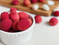 a white bowl filled with raspberries on top of a table next to a cutting board