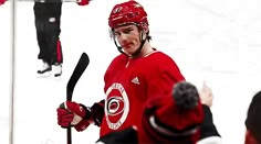 the hockey player is holding his stick in one hand and wearing a red jersey with white on it