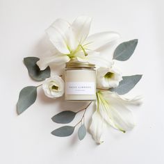 a candle with white flowers and leaves around it