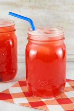 two mason jars filled with red liquid and blue straws on a checkered table cloth