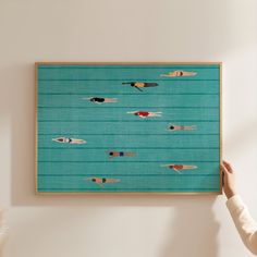 a person holding up a painting with people swimming in the water on blue boards above them