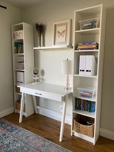 a white desk sitting in the corner of a room next to a book shelf and lamp