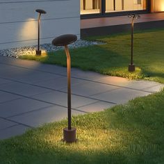 two lights that are in the grass near a building and some plants on the ground