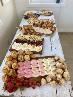 an assortment of pastries and desserts displayed on a long wooden table in front of a window