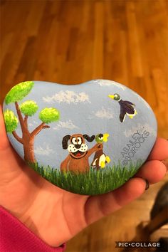 a hand holding a painted rock with animals on it