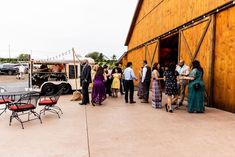 a group of people standing in front of a wooden building next to tables and chairs