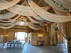 the inside of a barn decorated with white drapes and greenery on the ceiling