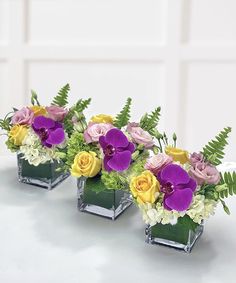 three square vases filled with different colored flowers and greenery on top of a table