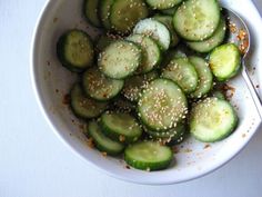 a white bowl filled with cucumbers covered in sesame seeds