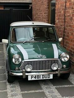 an old green and white car parked in front of a brick building