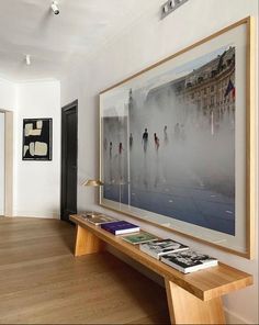 an art work hangs on the wall above a wooden bench in a room with hardwood floors