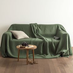 a couch covered in a green blanket next to a table with a camera on it