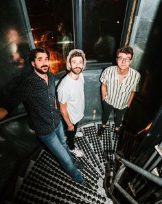 three men standing in front of a window at the top of a building with metal grates