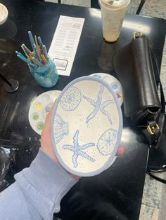 a person holding up a plate with starfishs on it and paintbrushes in the background