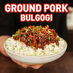 a person holding a bowl filled with food on top of a wooden table next to a sign that reads ground pork bulgoi