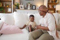 a woman sitting on top of a white couch next to a little boy