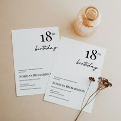 two white cards with black numbers on them sitting next to a vase filled with flowers