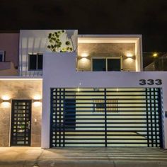 a white house with a black gate and lights on the front door is lit up at night