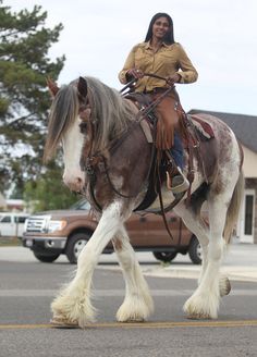 a woman riding on the back of a brown and white horse in a parking lot