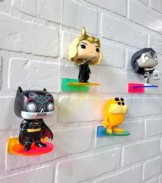 five funky little figurines are lined up against a white brick wall, one is black and the other is yellow