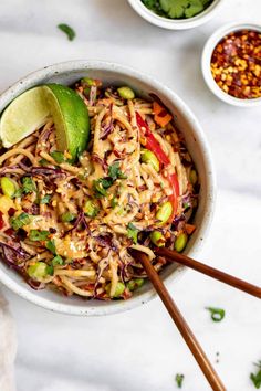 a bowl filled with noodles and vegetables next to two bowls of seasoning on the table