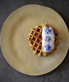 a waffle topped with icing and blue flowers on top of a yellow plate