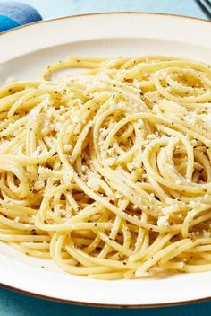 a white plate topped with pasta on top of a blue and white table cloth next to utensils