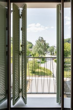 an open door leading to a balcony with green shutters on the outside and trees in the background