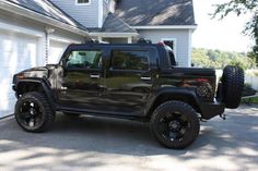 a black jeep is parked in front of a house with two large tires on it